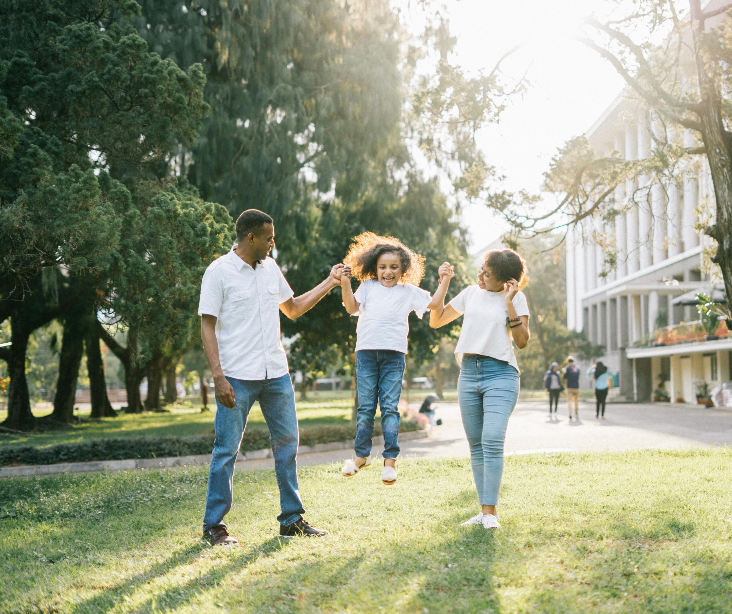 Parents joyfully swinging daughter between them in a sunny park.