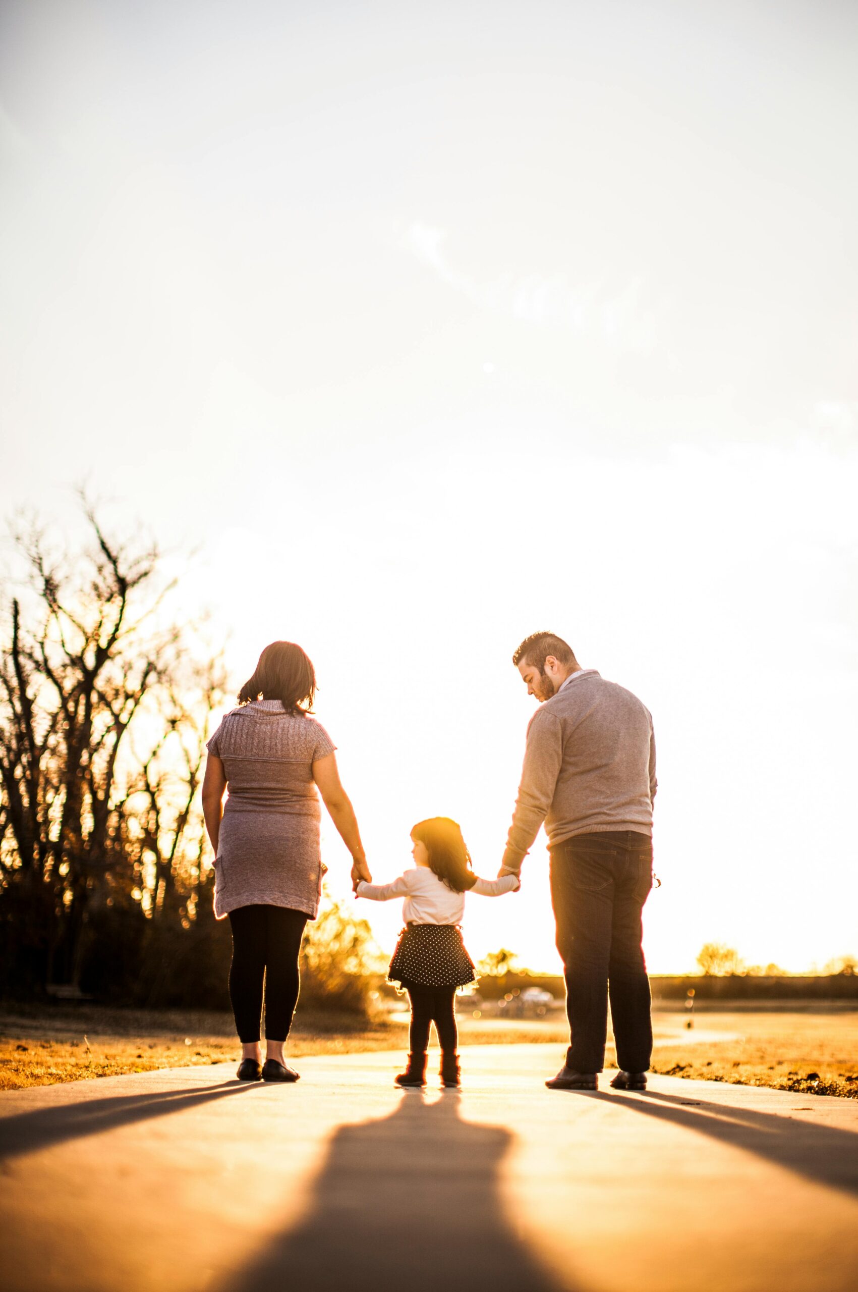 Parents holding hands with their daughter while walking at sunset.