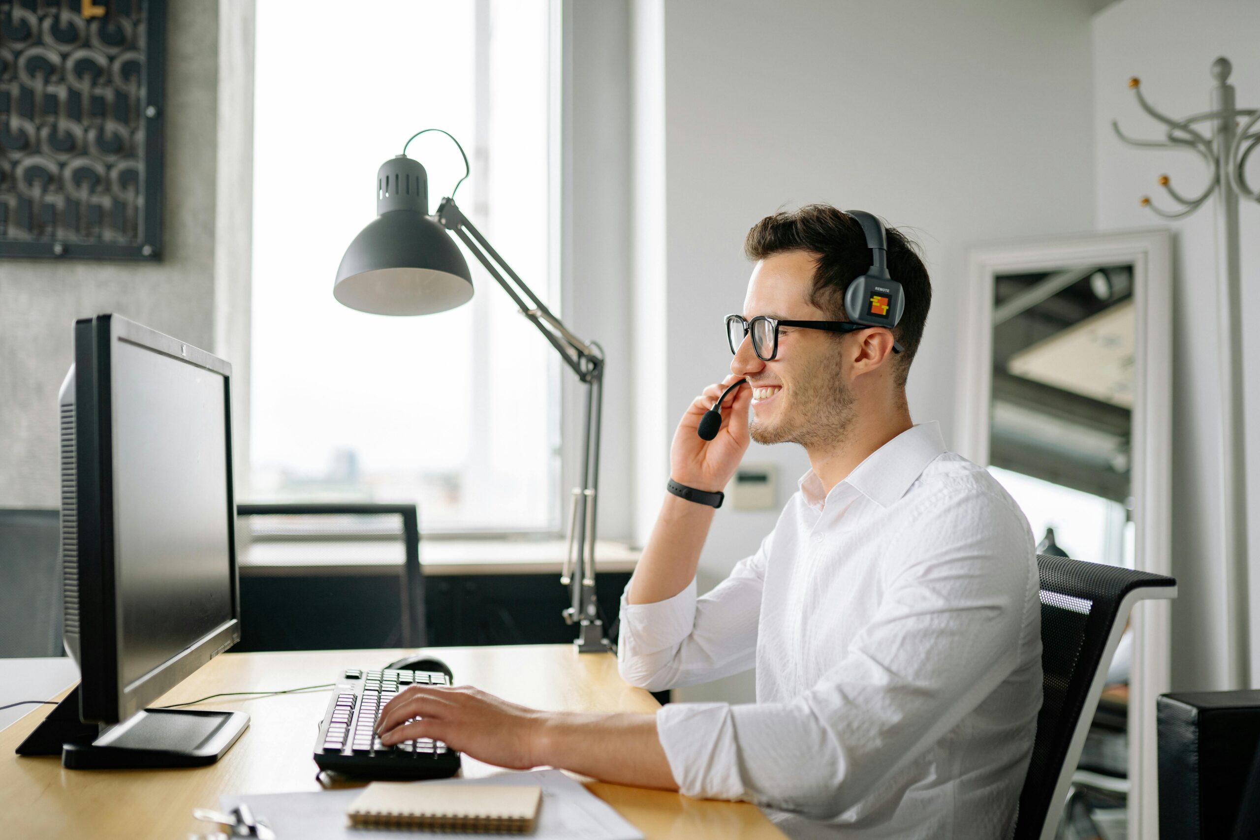 Man wearing headset smiling while working at computer desk.