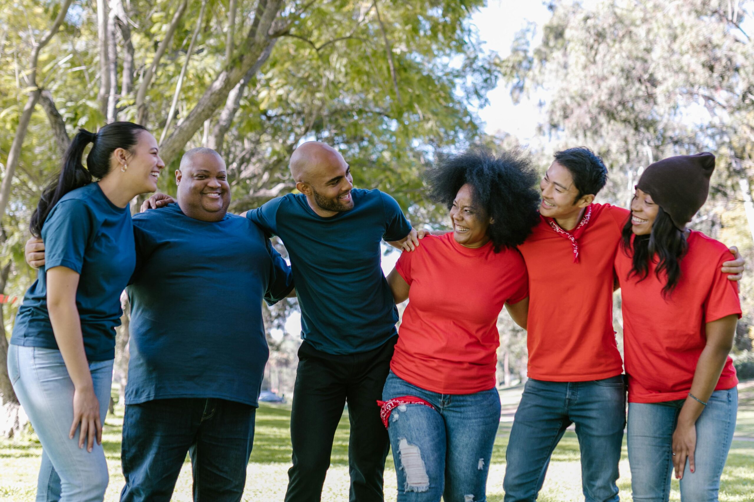 Group of six diverse adults smiling and embracing outdoors in a park.